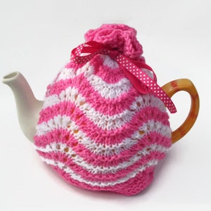 May include: Pink and white knitted teapot cozy with a white polka dot ribbon.