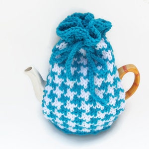 May include: A teal and white crocheted teapot cozy with a drawstring closure. The cozy is made with a chevron pattern.