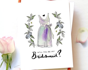 Puede incluir: Una tarjeta blanca con una ilustración dibujada a mano de un vestido de dama de honor azul claro y morado con una corona de flores verdes a su alrededor. El texto "Will you be my Bridesmaid?" está escrito en cursiva negra.