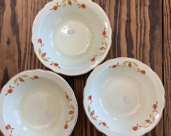 May include: Three off-white ceramic bowls with a scalloped edge and a gold rim. Each bowl features a repeating pattern of orange and brown floral designs. The bowls are arranged on a dark wooden surface.