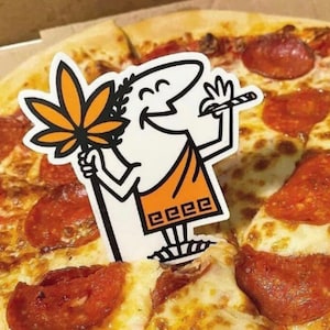Puede incluir: Una pizza con pepperoni y queso, cubierta con un personaje de dibujos animados que sostiene un palo con una hoja en él. El personaje lleva una túnica blanca con ribetes naranjas y el texto "EEEE" en la parte inferior.