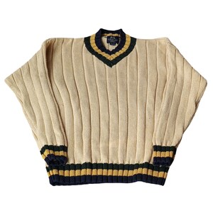 May include: Cream-colored ribbed knit sweater with a V-neck and long sleeves. The collar, cuffs, and hem feature navy blue, gold, and dark green stripes. The sweater has a relaxed fit.