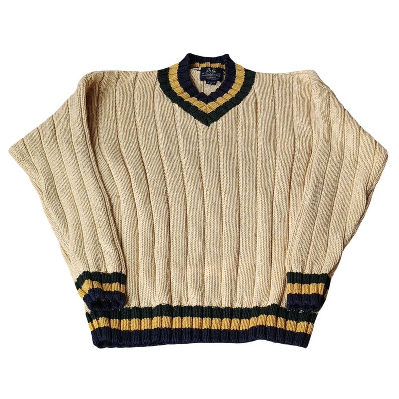 May include: Cream-colored ribbed knit sweater with a V-neck and long sleeves. The collar, cuffs, and hem feature navy blue, gold, and dark green stripes. The sweater has a relaxed fit.