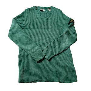 May include: A teal green ribbed knit sweater with a V-neck. The long-sleeved sweater has a small patch on the left sleeve. The label is visible at the neckline. The sweater is made of a soft, comfortable material.