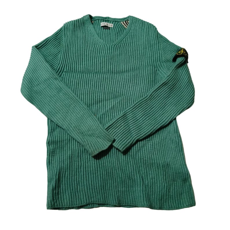 May include: A teal green ribbed knit sweater with a V-neck. The long-sleeved sweater has a small patch on the left sleeve. The label is visible at the neckline. The sweater is made of a soft, comfortable material.