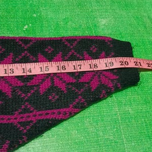 May include: Close-up of a section of a black and magenta patterned sweater. A pink measuring tape shows a length of approximately 12 to 24 inches. The sweater has a repeating floral design.