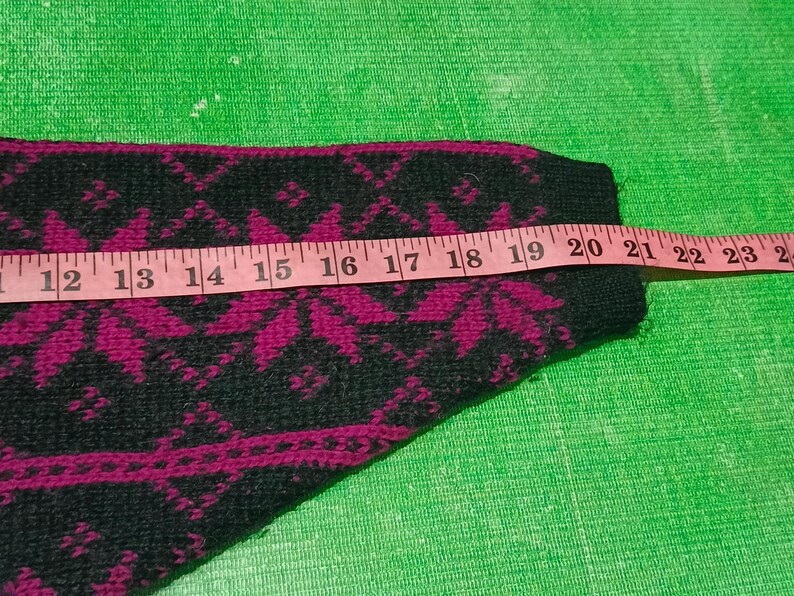 May include: Close-up of a section of a black and magenta patterned sweater. A pink measuring tape shows a length of approximately 12 to 24 inches. The sweater has a repeating floral design.