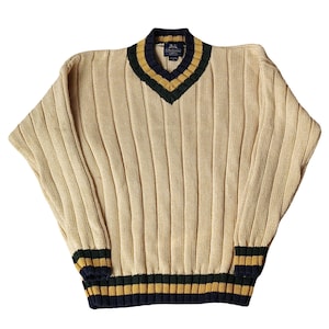 May include: Cream-colored ribbed knit sweater with a V-neck. The collar, cuffs, and hem feature navy blue, gold, and green stripes. The sweater has a relaxed fit and long sleeves.
