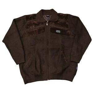 May include: A brown zip-up sweater with a ribbed knit design. The sweater features suede-like patches on the chest and shoulders, a collar, and two front pockets. A small label is sewn on the chest. The sweater is a medium size.