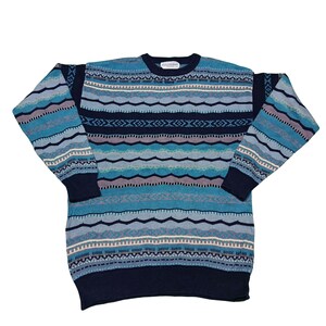 Könnte beinhalten: Ein blauer Rundhals-Pullover mit Muster. Der Pullover hat horizontale Streifen in Blau-, Grau- und Weißtönen. Die Bündchen und der Saum sind in einem dunkleren Blauton gehalten. Der Pullover ist aus weichem Strickmaterial.