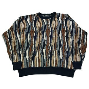 Peut inclure: Un pull à col rond avec un motif unique dans les tons de marron, beige, bleu et blanc. Le pull a un col, des poignets et un ourlet bleu marine foncé. Le motif est un design vertical répétitif.