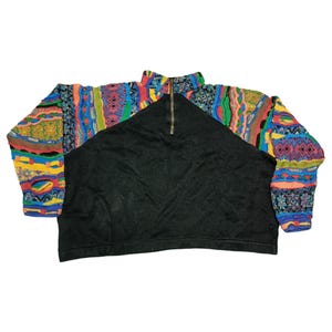 Peut inclure: Un pull noir à fermeture éclair quart de col avec des manches aux motifs colorés. Les manches présentent un mélange de motifs géométriques et floraux dans les tons de bleu, rouge, vert et jaune. Le pull a un col montant et une fermeture éclair dorée.