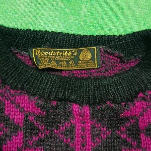May include: Close-up of a vintage Nordstrikk sweater. The sweater features a black crew neck and a pattern of magenta and black geometric shapes. A tag with the brand name and origin is visible.