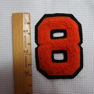 May include: Orange felt number eight with black outline. The number is approximately 2 inches tall.