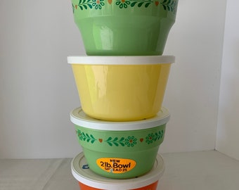 May include: A set of four vintage plastic mixing bowls with lids. The bowls are stacked in order of size, with the largest bowl on the bottom. The bowls are green, yellow, and orange. The largest bowl has a green floral design and a sticker that reads "New 2 lb. Bowl Spread 25".