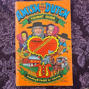 May include: An orange-covered Amish Dutch Tourist Guide with illustrations of Amish people and a horse-drawn carriage. The guide includes 9 maps and 15 pages for coloring. The cover features the text "Amish Dutch Tourist Guide" and "Pennsylvania Dutch Country".