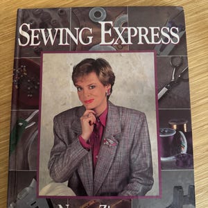 May include: A book titled "Sewing Express" by Nancy Zieman. The cover features a woman in a gray blazer and a red shirt, with sewing-related imagery in the background.