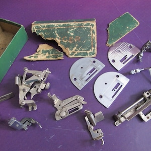 May include: A collection of vintage sewing machine parts, including a foot pedal, a needle plate, and a bobbin case. The parts are made of metal and have a silver finish. The parts are arranged on a purple surface. The parts are in good condition and show signs of age.