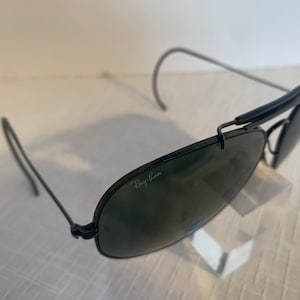 May include: Black Ray-Ban aviator sunglasses with green lenses. The sunglasses have a metal frame and a folding design.