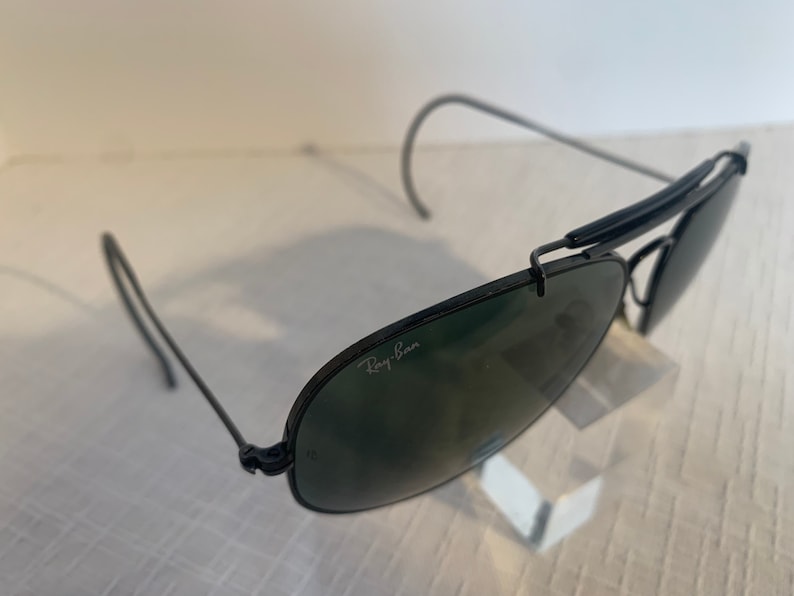 May include: Black Ray-Ban aviator sunglasses with green lenses. The sunglasses have a metal frame and a folding design.