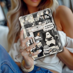 May include: A tablet case with a Halloween theme, featuring a black and white design. The case shows a ghost reading a book, a fireplace, and the text "MY WEEKEND IS ALL BOO-KED UP". Other elements include a black cat, pumpkins, and a spider web.