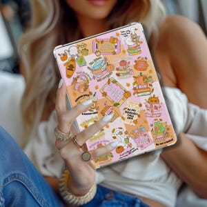 以下が含まれることがあります： 秋をテーマにしたデザインのタブレットケース。ケースは、カボチャ、本、「Pumpkin Spice」や「Bookish Vibes」などのフレーズなど、さまざまなイラストが描かれたピンクとオレンジの背景が特徴です。