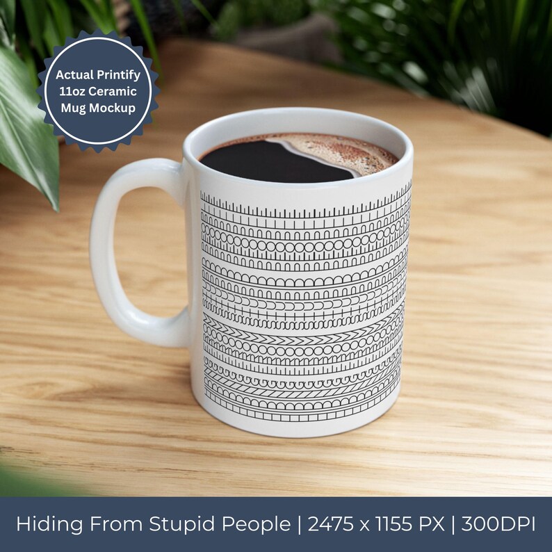 Op de afbeelding: Witte keramische mok met een zwart-wit geometrisch patroon en de tekst "Hiding From Stupid People". De mok is gevuld met donkere vloeistof en staat op een houten oppervlak. De mok is gelabeld als een 325 ml keramische mok.