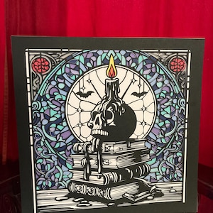 May include: A black and white illustration of a skull with a candle on top of a stack of books. The illustration is framed in a stained glass style with blue, purple, and green colours.