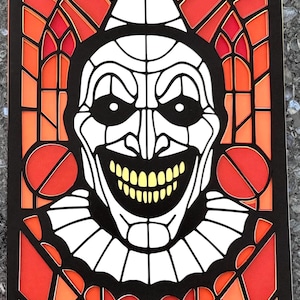 May include: A paper art piece depicting a clown's face in a stained-glass style. The design uses black, white, orange, and red. The clown has a wide grin, a white ruffled collar, and a pointed hat. The artwork is layered for depth.