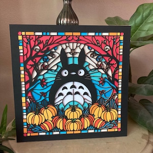 May include: A layered paper art piece featuring a black Totoro character surrounded by pumpkins and a stained-glass style background. The artwork has a black border and uses vibrant colors like orange, red, blue, and yellow.