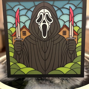 May include: A framed, layered art piece featuring the Ghostface character from the Scream horror film series. The artwork depicts Ghostface holding two bloody knives against a backdrop of a blue sky, houses, and green foliage.