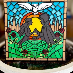 May include: A layered art piece depicting a couple holding hands in front of a yellow sun, with a maze, roses, and castle silhouettes. A white owl and dove are at the top, with a stained-glass style background of blue, orange, and green.