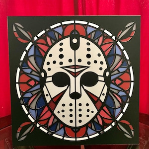 May include: A black and white hockey mask with a stained glass design in red, blue, and gray. The mask is surrounded by a circular design with a black background.