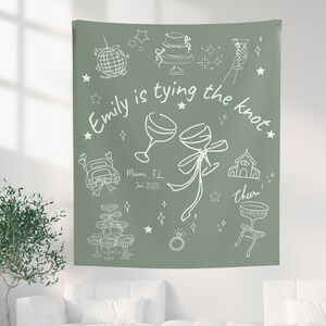 May include: Sage green tapestry with white line art illustrations of wedding-related icons, including a cake, champagne glasses, and a car. Text reads "Emily is tying the knot" with the date and location.