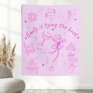 May include: A light pink tapestry with a hand-drawn design in a darker pink. The text "Emily is tying the knot" is featured, along with illustrations of a disco ball, cake, champagne glasses, and a wedding ring. The date "Jul 2025" is also included.