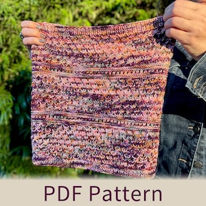 May include: A hand-knitted cowl in shades of pink, purple, and orange with a textured stitch pattern. The cowl is held up, showcasing the intricate design and color variations. The text "PDF Pattern" is displayed at the bottom.