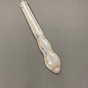 May include: A silver seam ripper with a decorative handle and a red ball at the tip. The tool is designed for removing stitches and is made of metal. The handle has an ornate floral design.