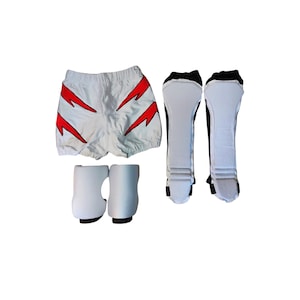 Puede incluir: Pantalones cortos blancos de artes marciales con diseños de rayos rojos, junto con equipo de protección blanco y negro para espinillas y pies. El conjunto incluye espinilleras y protectores de pies, diseñados para deportes de combate.