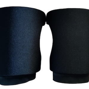 May include: A pair of solid black knee pads featuring a contoured, flexible design with a smooth, matte exterior finish. These protective sleeves are constructed with a thick, padded central section and reinforced elastic bands at the top and bottom.