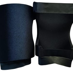 May include: A pair of black knee pads featuring a smooth, solid-colored exterior fabric and a contoured shape. The interior side displays a structured design with wide, horizontal elastic bands at the top and bottom edges for secure placement.