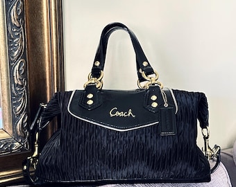 May include: Black Coach handbag with gold-tone hardware. The bag features a pleated design and a patent leather top with the Coach logo in gold. Includes a detachable shoulder strap and a Coach hang tag.