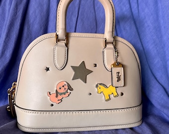 Borsa a mano Coach Revel 24 in pelle color avorio, personalizzata con spille smaltate Coach.