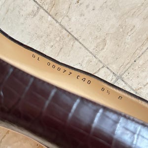 May include: Close-up of a brown leather shoe with a crocodile pattern. The shoe has the size 8 1/2 B and the number C40 printed on the insole. The shoe is on a light-colored surface.