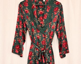 May include: A dark green floral robe with red roses and green lace trim. The robe has long sleeves and a matching tie belt. The robe is hanging on a black hanger.
