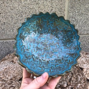 Puede incluir: Un cuenco de cerámica azul turquesa con un borde ondulado y un patrón de hojas de marihuana verdes en relieve.