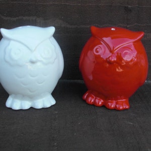 Peut inclure: Deux figurines d'hibou en c&eacute;ramique, l'une blanche et l'autre rouge. Les hiboux ont des yeux noirs et des becs.