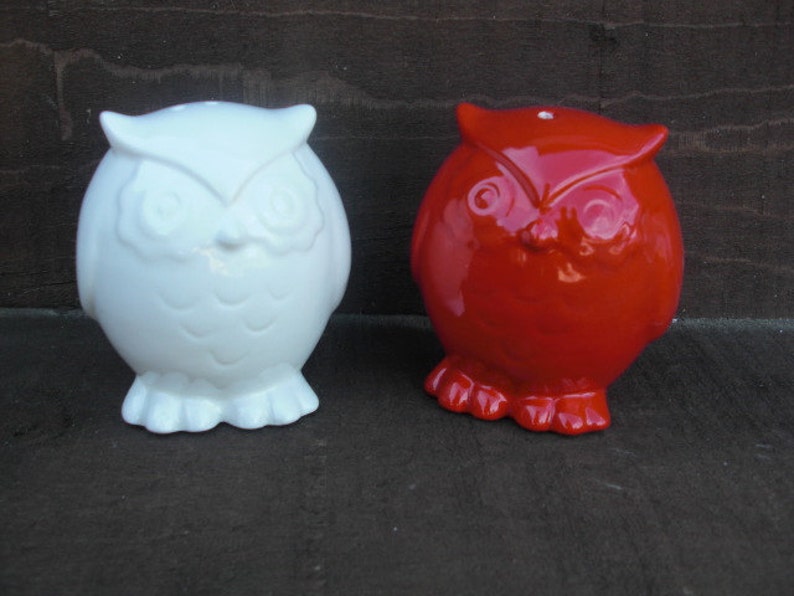 Peut inclure: Deux figurines d'hibou en c&eacute;ramique, l'une blanche et l'autre rouge. Les hiboux ont des yeux noirs et des becs.