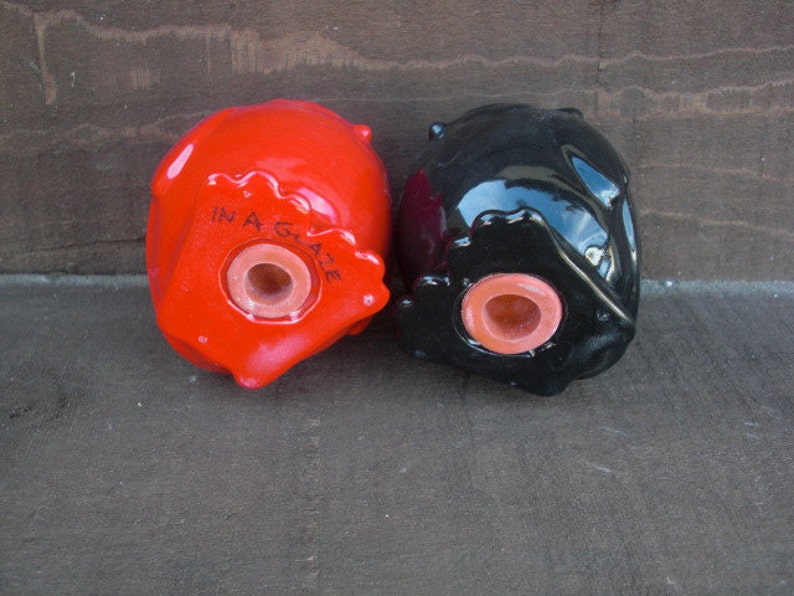 Peut inclure: Une paire de sali&egrave;res et poivri&egrave;res en c&eacute;ramique en forme de t&ecirc;tes. La sali&egrave;re est rouge et porte l'inscription "In A Gaze" au fond. Le poivrier est noir.