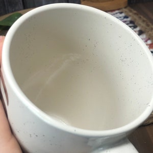 May include: White ceramic mug with a speckled finish. The mug is empty and has a wide, round opening.