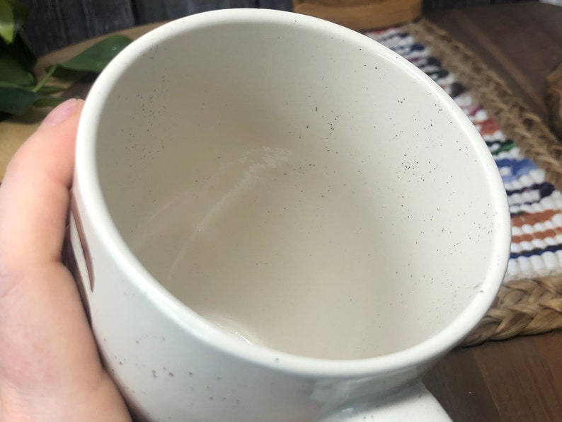 May include: White ceramic mug with a speckled finish. The mug is empty and has a wide, round opening.